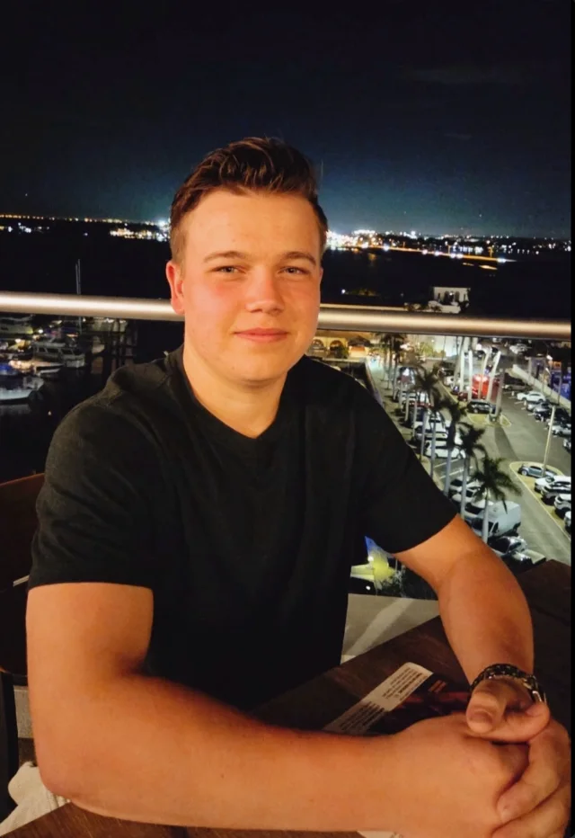 Jaron Zimmerman seated at a table on a balcony overlooking a marina at night