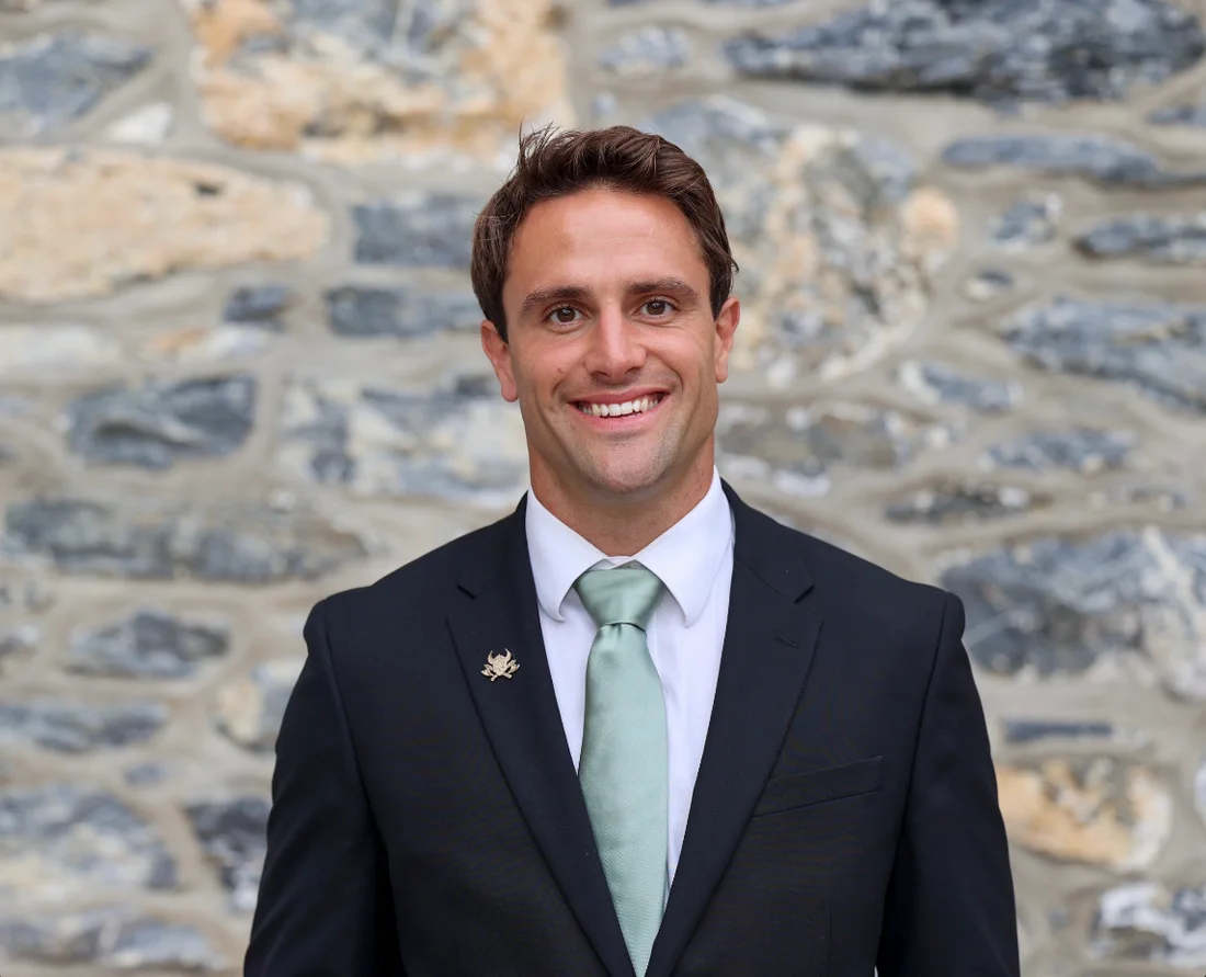 Lance Burkholder in a suit and tie, smiling in front of a stone wall